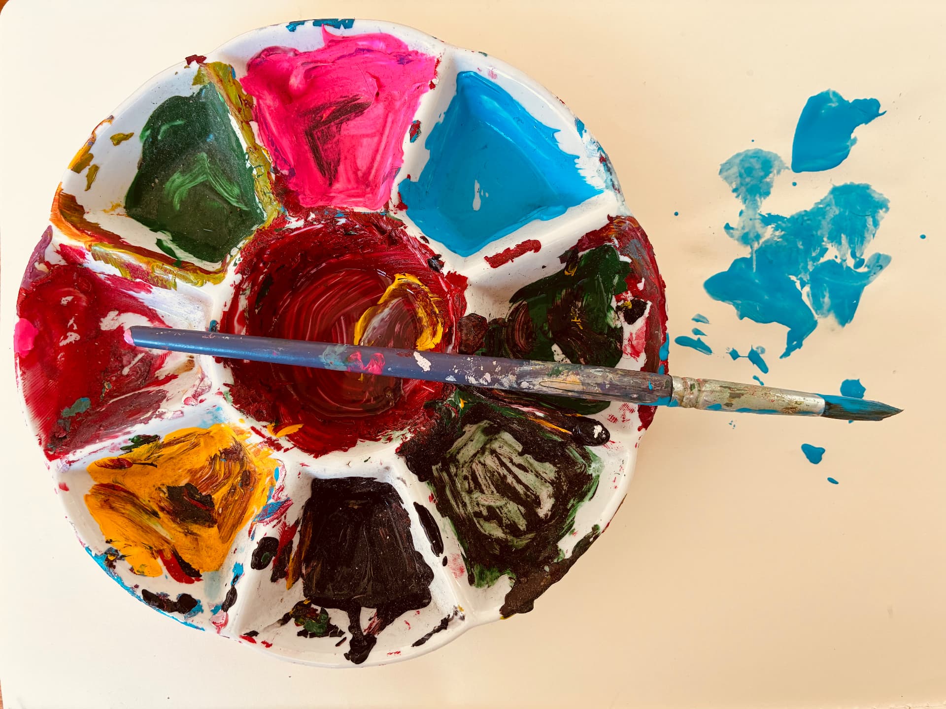 A used paint palette with bright colours and a brush resting across it